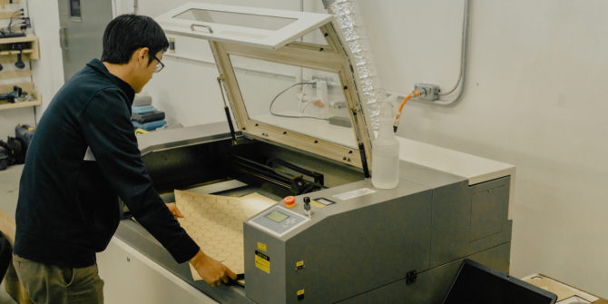 a man is opening the lid of a large laser cutter machine.