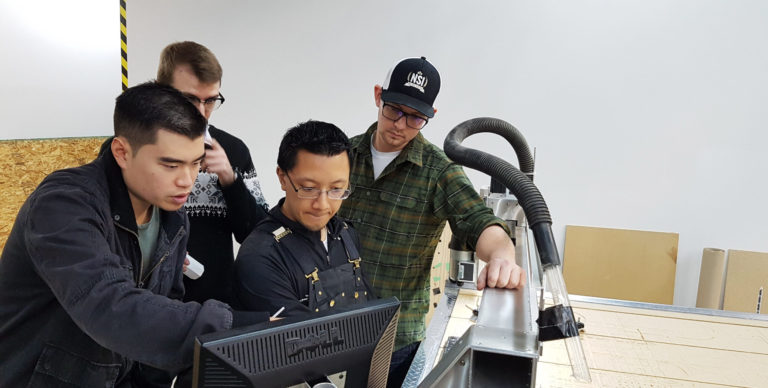 a group of people stand around a computer screen and CNC machine