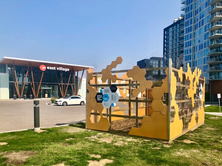 A yellow metal sculpture in a square sits in near the East Village visitor centre.