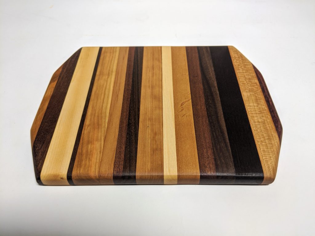 a product shot of a cutting board made of wood. the cutting board has stripes of different colored wood.