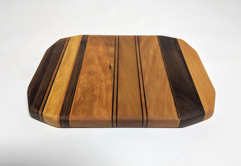 a wood cutting board made with joinery in different colors of wood in stripes.