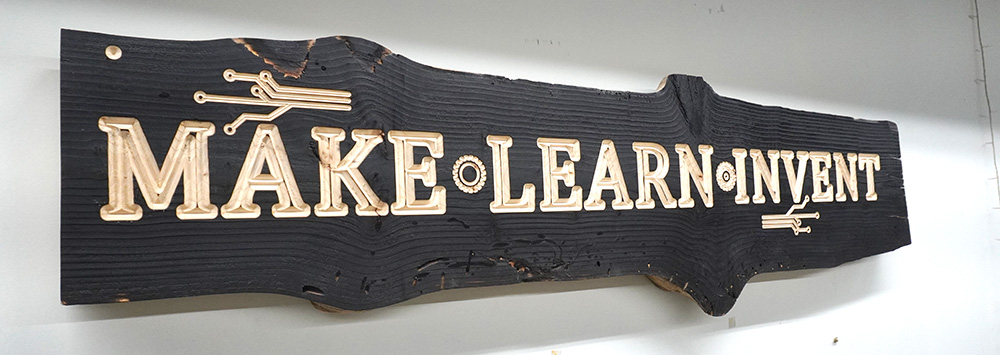 live edge wood with laser engraving that says Make Learn Invent with a burned black background. Create at Fuse 33 makerspace with a thunder laser- buy your own