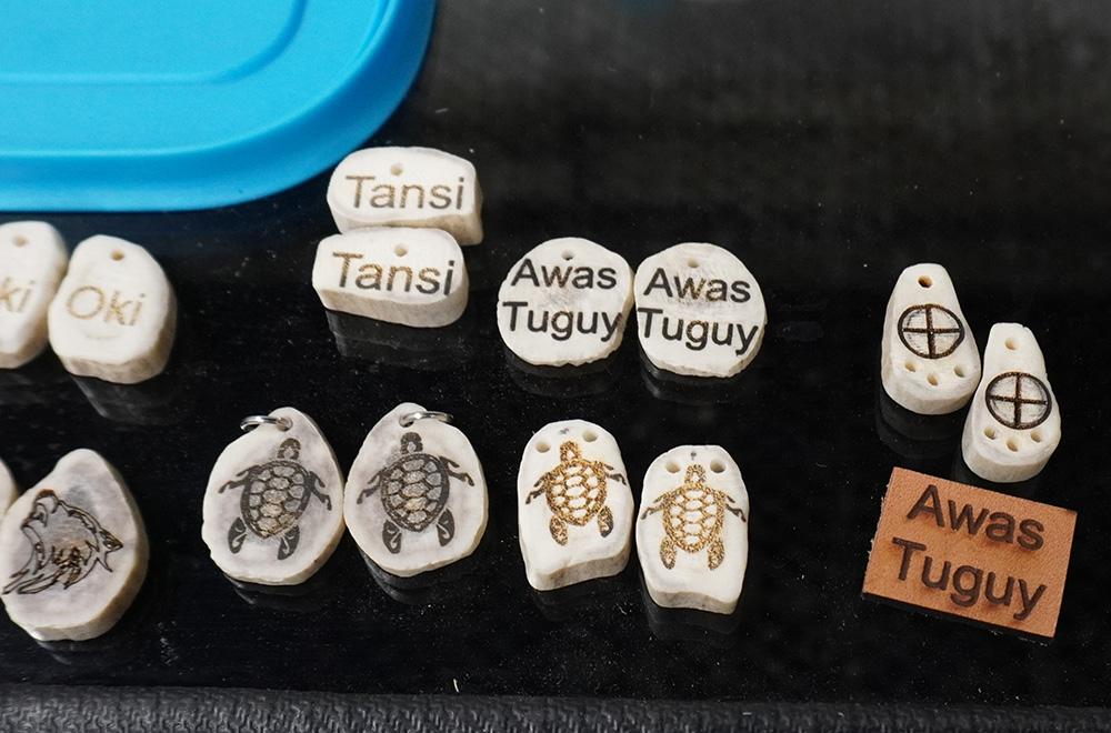 closeup of antlers and stones laser etched with pictures of turtles and the word Tansi and Awas Tuguy