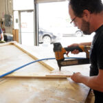 2 volunteers build a wooden triangle on a works bench at Fuse 33 makerspace. One uses a nail gun to attach braces on the corners